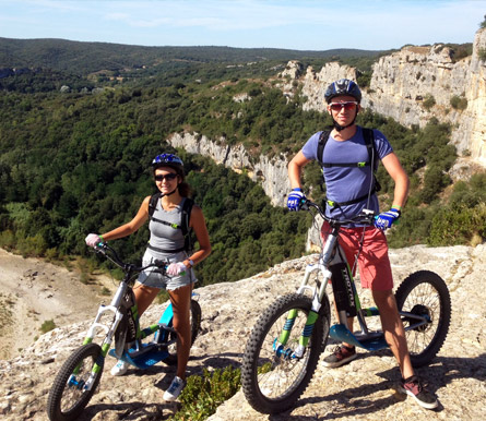 Un homme et une femme posent avec leur e-scoot devant une falaise dans les Cévennes