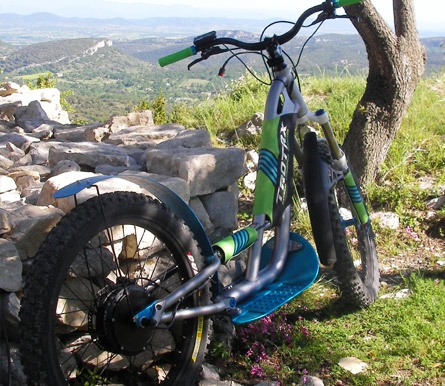 E-scoot Rando Escape posé contre un petit muret, un beau paysage vallonné du Gard en arrière-plan